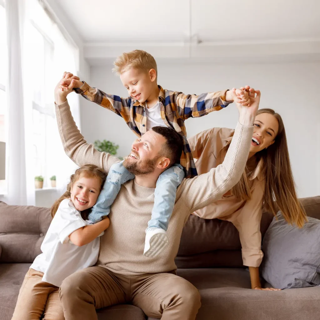 A family with great teeth, smiling and happily holding hands together in their living room.